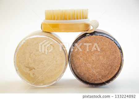 Two jars of body scrubs, one creamy and one coarse, paired with a wooden brush, highlighting natural skincare products for a refreshing and rejuvenating routine 133224892