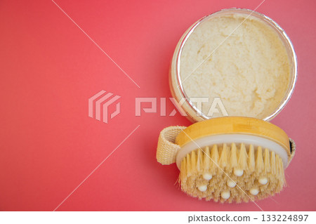 Body scrub in silver container paired with a natural bristle brush on a bright pink backdrop, emphasizing indulgent self-care and beauty routines 133224897
