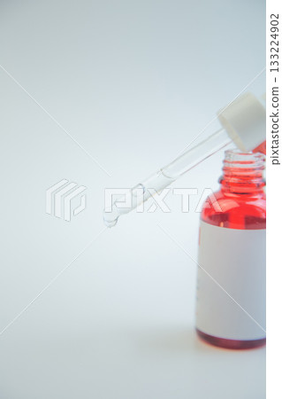 Dropper filled with vibrant red liquid hovers above a glass bottle, emphasizing skincare product design with a clean background, perfect for marketing and branding 133224902