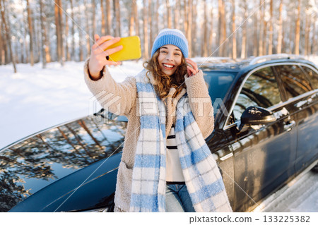 Young woman taking selfie photo, standing near the car while traveling in road trip. Winter holidays Young woman taking selfie photo, standing near the car while traveling in road trip. Winter holidays 133225382