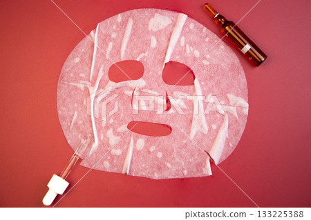 Flat lay of pink facial mask, dropper bottle, and amber serum on red backdrop, highlighting skincare products for beauty routines and self-care moments Flat lay of pink facial mask, dropper bottle, and amber serum on red backdrop, highlighting skincare products for beauty routines and self-care moments 133225388