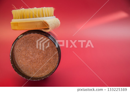 Body scrub in a black jar with a wooden brush on top, placed against a bright red background, highlighting skincare and wellness for self-care practices 133225389