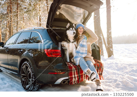 Woman with husky dog have picnic in car trunk near pine forest, traveling by car. Travel concept. Woman with husky dog have picnic in car trunk near pine forest, traveling by car. Travel concept. 133225500