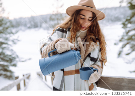 Young woman drinks hot tea while holding a thermos in nature. . Vacation concept 133225741