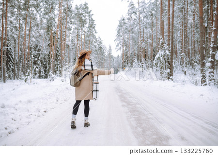 Beautiful young woman in winter forest is waiting for a car. Hitchhiking in winter. Great snowy day. Beautiful young woman in winter forest is waiting for a car. Hitchhiking in winter. Great snowy day. 133225760