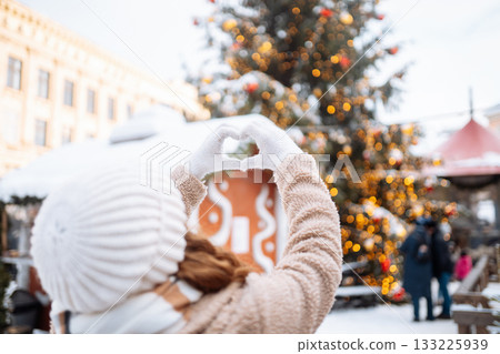 Young woman holding hands in the shape of a heart against the background of a Christmas tree. Young woman holding hands in the shape of a heart against the background of a Christmas tree. 133225939