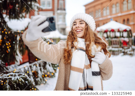 Young tourist uses a smartphone while walking through a Christmas market. Young tourist uses a smartphone while walking through a Christmas market. 133225940