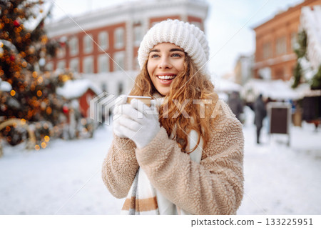 Woman is having fun at a street holiday fair, drinking a hot drink. Winter holidays. Lifestyle. 133225951