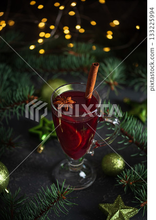 Glass of Mulled Wine with Cinnamon Surrounded by Christmas Decor and Lights 133225994