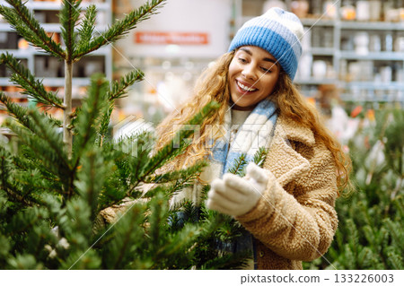 Young woman buys Christmas tree at fair. She chooses beautiful Christmas tree for her home interior. 133226003