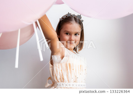 Smiling caucasian female child with balloons and star headband 133226364