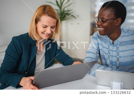 Diverse businesswomen collaborating and smiling during office meeting Diverse businesswomen collaborating and smiling during office meeting 133226632