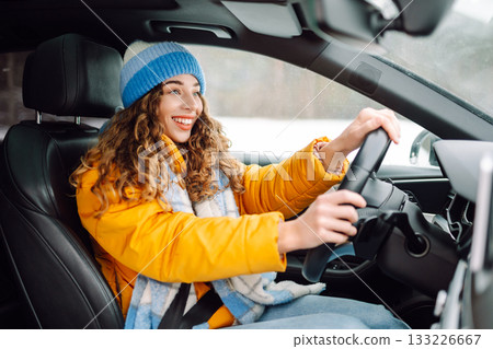 Happy woman in winter outfit driving car. The concept of transport, lifestyle. 133226667