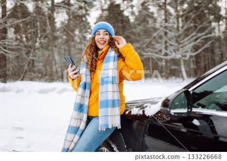 Young woman with phone near her car in a winter forest. Sending messages, communicating with friends Young woman with phone near her car in a winter forest. Sending messages, communicating with friends 133226668