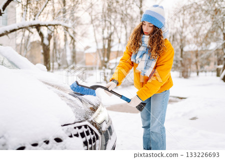 Woman cleaning snow off car during winter snowfall with brush. Scraping ice. Winter cleaning car. Woman cleaning snow off car during winter snowfall with brush. Scraping ice. Winter cleaning car. 133226693