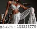 Dancer in sparkling outfit posing confidently beside drum set 133226775