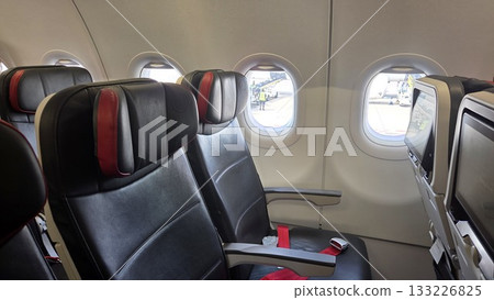 Comfortable airplane cabin interior with empty passenger seats and window views Comfortable airplane cabin interior with empty passenger seats and window views 133226825