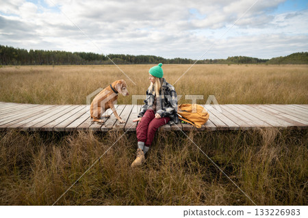 Serious woman owner training hunting dog with commands on eco boardwalk over autumn peat bog Serious woman owner training hunting dog with commands on eco boardwalk over autumn peat bog 133226983