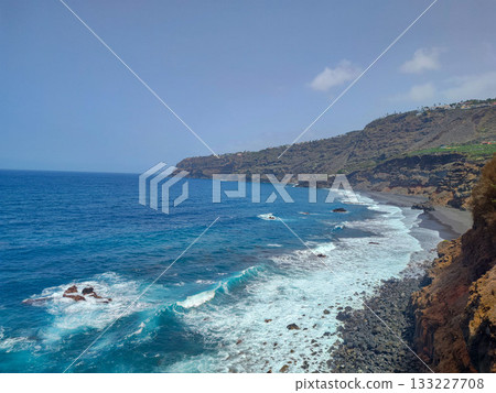 Experience the breathtaking coastal view, featuring vibrant blue waters alongside a rocky shoreline 133227708