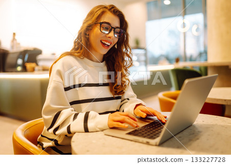 Young woman sitting on cafe with laptop. Beautiful college student on a cafe. Concept for education Young woman sitting on cafe with laptop. Beautiful college student on a cafe. Concept for education 133227728