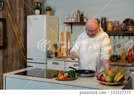 Senior man preparing vegetables, Elderly gentleman cooking with focus, Older man slicing produce in cozy kitchen, Senior male chef chopping vegetables in warm environment 133227775