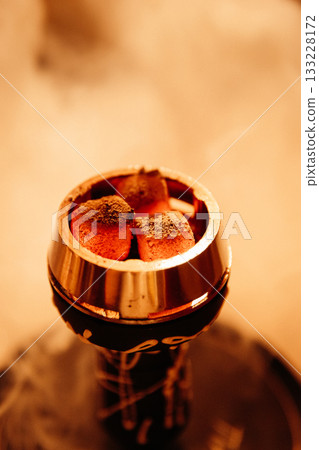 Glowing hookah coals in a metal bowl, warm bokeh bar lighting, macro closeup 133228172