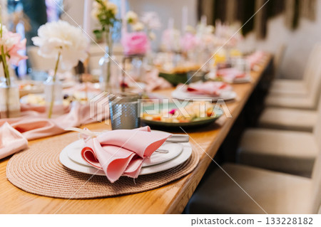 Elegant place setting with pink napkin and floral decor at festive banquet table Elegant place setting with pink napkin and floral decor at festive banquet table 133228182