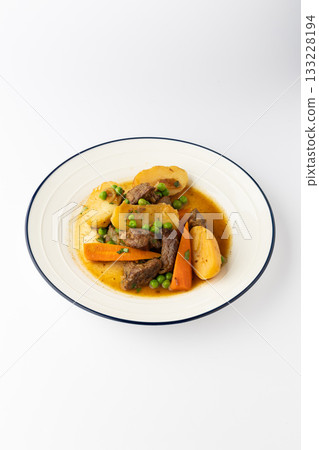 Beef stew with potatoes, carrots and peas in rich gravy on a white plate 133228194