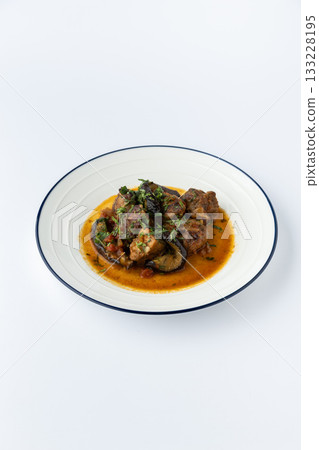 Beef stew with eggplant in tomato sauce, garnished with herbs, studio plate on white Beef stew with eggplant in tomato sauce, garnished with herbs, studio plate on white 133228195