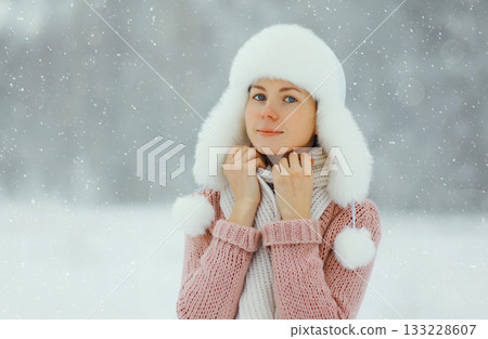 Young woman outdoors, girl in winter hat, sweater on snowy forest background with snowflakes 133228607