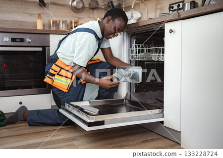 Plumber fixing a dishwasher in a kitchen 133228724