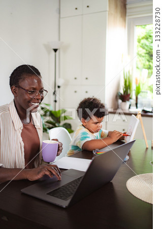 Black mother working from home with child drawing 133228730