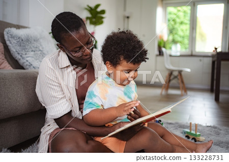 Black mother reading book with toddler son at home 133228731