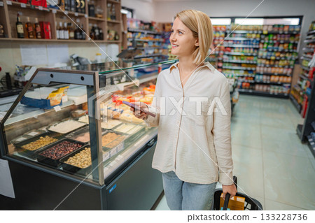 Woman shopping for groceries, using phone in supermarket Woman shopping for groceries, using phone in supermarket 133228736