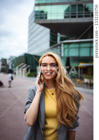 Businesswoman talking on phone outdoors in city smiling 133228756