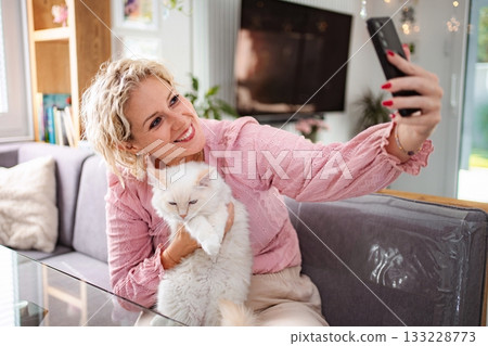 Woman and cat taking selfie with smartphone in living room 133228773