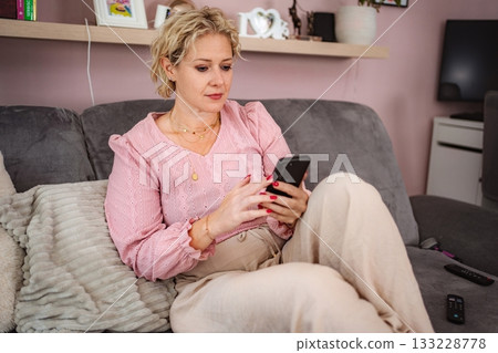 Woman relaxing at home using smartphone on sofa Woman relaxing at home using smartphone on sofa 133228778