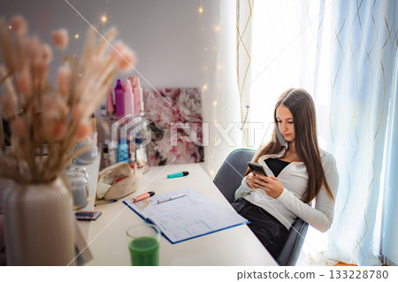 Teenager using phone at desk procrastinating homework 133228780