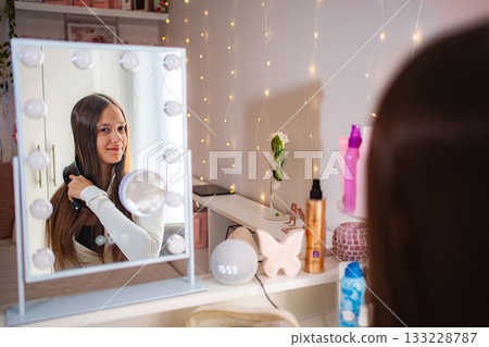 Teenager brushing long hair in illuminated vanity mirror 133228787