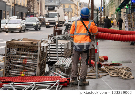 A worker in a hard hat sets up scaffolding on a busy street in the city center. A worker in a hard hat sets up scaffolding on a busy street in the city center. 133229003