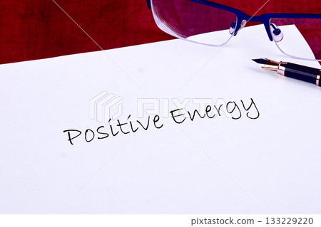 A calm workspace showcases the phrase Positive Energy written on a sheet of paper. Glasses and a pen lie nearby, promoting a sense of creativity and motivation during a bright afternoon 133229220