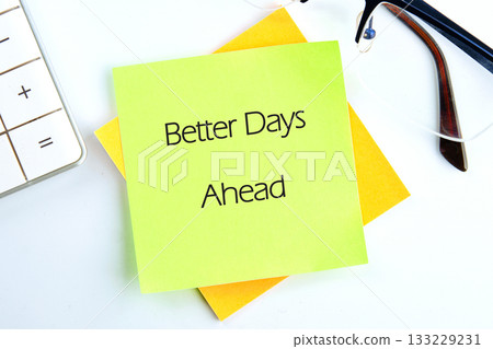 A vibrant green sticky note with the words Better Days Ahead stands out on a desktop. Nearby, a calculator and glasses complete the picture, reflecting a workspace filled with optimism 133229231