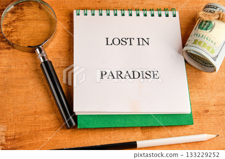 A green notebook sits open with the phrase lost in paradise written prominently. Alongside it are a magnifying glass and a rolled bill, creating an atmosphere of exploration and wonder 133229252