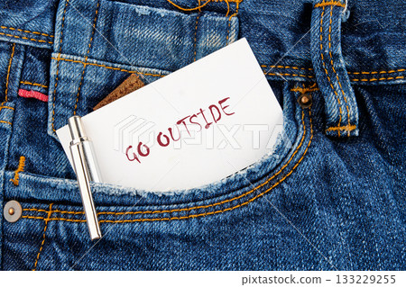 A note with the words go outside peeks from a blue denim pocket. The setting suggests a casual day, promoting adventure and the joy of exploring nature. Perfect for outdoor enthusiasts A note with the words go outside peeks from a blue denim pocket. The setting suggests a casual day, promoting adventure and the joy of exploring nature. Perfect for outdoor enthusiasts 133229255