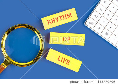 Colorful yellow letters spelling rhythm of life are arranged next to a magnifying glass on a vibrant blue surface. This scene invites reflection on lifes patterns and experiences 133229296