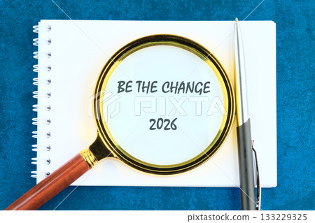 A magnifying glass rests on a blank notebook, highlighting the words Be the change alongside the year 2026, symbolizing the importance of taking initiative for a better future A magnifying glass rests on a blank notebook, highlighting the words Be the change alongside the year 2026, symbolizing the importance of taking initiative for a better future 133229325