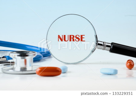 A focused nurse inspects colorful medicine pills through a magnifying glass. A stethoscope and a silver medical device are nearby, highlighting attention to health details A focused nurse inspects colorful medicine pills through a magnifying glass. A stethoscope and a silver medical device are nearby, highlighting attention to health details 133229351