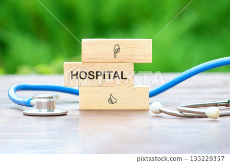 Stacked wooden blocks spell out hospital next to a stethoscope, symbolizing healthcare and wellness in a calm outdoor environment. Nature adds tranquility to the scene 133229357