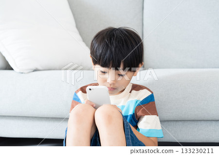 Elementary school boy playing with smartphone in the living room Elementary school boy playing with smartphone in the living room 133230211