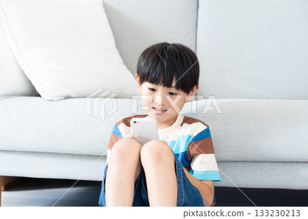 Elementary school boy playing with smartphone in the living room Elementary school boy playing with smartphone in the living room 133230213